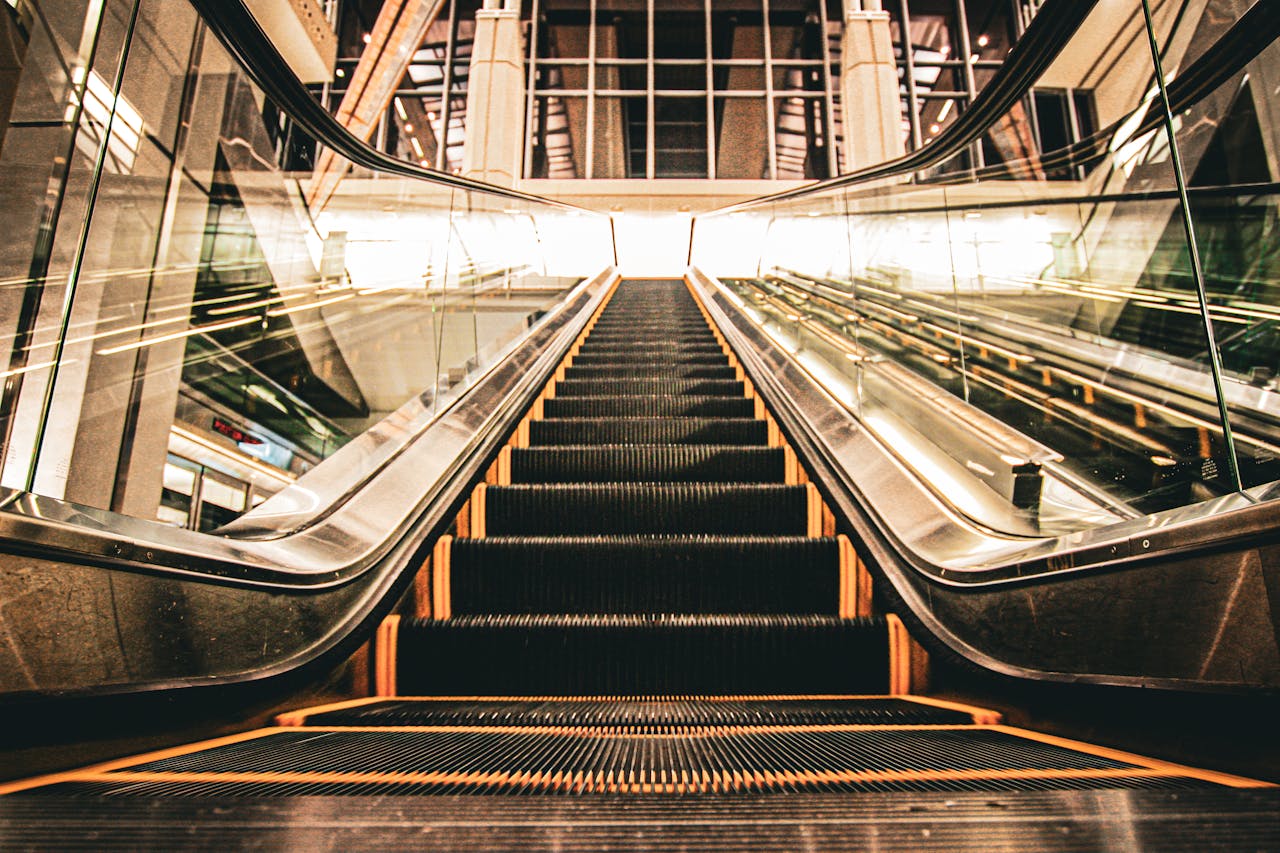 A low angle view of an illuminated airport escalator with glass and metal elements.